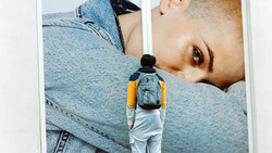 Person wearing backpack standing before large-scale portrait photography installation.