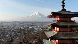 Red pagoda with snow-capped mountain peak in the distance beyond a sprawling city landscape.