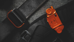 Orange and black camera equipment arranged on gray fabric with dramatic side lighting.