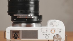 Top-down view of a white mirrorless camera with a large black telephoto lens mounted, showing controls and aperture ring.