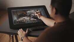 Photographer using stylus on graphics tablet displaying color grading interface with video footage.