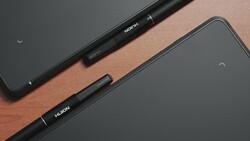 Two black stylus pens labeled with text, arranged diagonally on a wooden surface next to tablet devices.