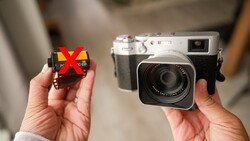 Hands holding a vintage rangefinder camera and an old film cartridge marked with a red X.
