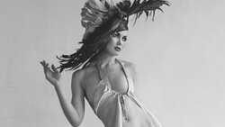 Woman in halter top with dramatic feathered headpiece, shot against neutral background in black and white.
