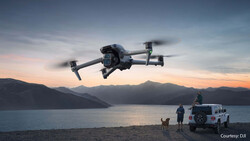 Drone hovering above a beach at sunset with people and a vehicle below.