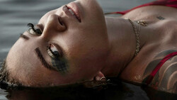 Male portrait with head tilted back, eyes closed, wearing chain necklace in shallow water.