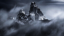 Snow-covered jagged mountain peaks rising through thick clouds under a dramatic gray sky.