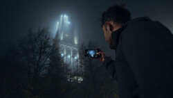 Photographer capturing a Gothic cathedral shrouded in fog at night with a smartphone.