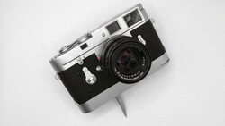 Vintage rangefinder camera with chrome top plate and black body on white background.