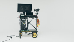 Mobile teleprompter rig on yellow-wheeled cart with monitor displaying timecode display.
