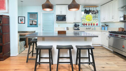 Modern kitchen with white cabinetry, dark wood island with three black stools, and pendant lights overhead.