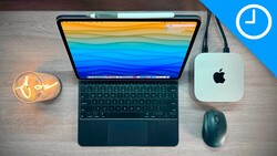 Flat lay of a tablet with colorful wallpaper, wireless mouse, Mac mini, and desk lamp on wood surface.