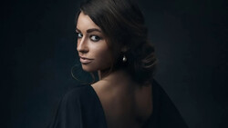Woman with dark hair looking over shoulder against dark background.