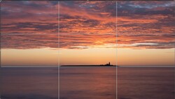 Seascape at sunset with a distant lighthouse silhouette centered on the horizon beneath dramatic orange and purple clouds.