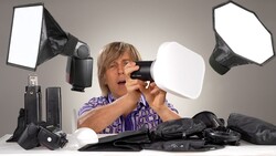Photographer examines camera flash and softbox diffuser among studio lighting equipment.