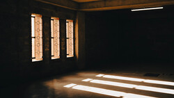 Sunlight streaming through three narrow windows into a dark interior space, creating geometric shadows on the floor.