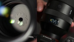 Close-up of a Sony lens showing aperture blades and focal length markings, held in natural lighting.