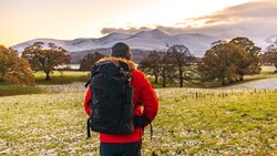 Hiker with backpack standing in a flooded field facing snow-capped mountains at sunset.