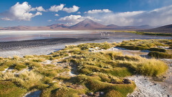Salt flat landscape with volcanic mountain peak under blue sky and white clouds.