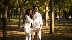 Couple walking together through a tree-lined park during golden hour.