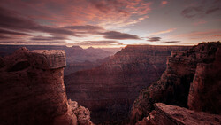 Grand Canyon vista at sunset with layered red rock formations and dramatic pink-orange sky.