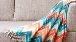Colorful geometric patterned throw blanket draped over a beige linen sofa.