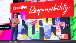Speaker presenting on stage in front of colorful abstract artwork with "Creative Responsibility" text overlay.