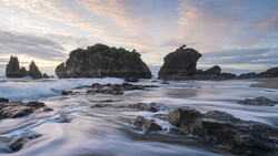 Rocky islands rising from turbulent ocean waves at dusk, with smooth water motion blur in foreground.