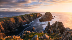 Dramatic coastal cliffs with jagged rock formations rising from turbulent ocean waves at golden hour.