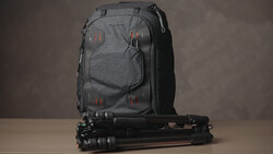Gray camera backpack with red accent straps positioned next to a black tripod on a neutral surface.