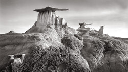 Dramatic black and white landscape of distinctive rock formations with flat-topped peaks rising from eroded badlands terrain.