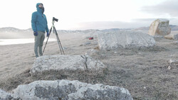 Photographer with tripod-mounted camera documenting rocky terrain in arid landscape.