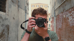 Photographer holding a Fujifilm mirrorless camera up to his face in a narrow urban alleyway.