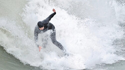 Surfer in black wetsuit riding a large wave with significant white water and spray.