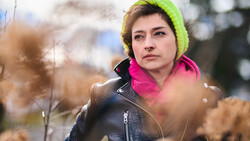 Woman in neon yellow beanie and magenta jacket looking away in autumn setting.