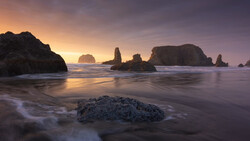 Rocky sea stacks silhouetted against a golden sunrise over calm ocean water.