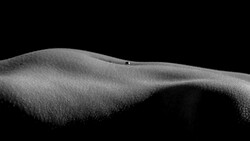 Monochromatic close-up of textured sand dunes with undulating ridges and a small figure visible on the crest.