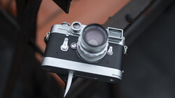 Vintage rangefinder camera with chrome and black body held in hands against dark clothing.
