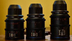 Three black cinema prime lenses with red markings arranged side-by-side against a yellow background.
