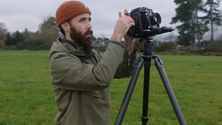 Bearded photographer operating a large format camera on a tripod in an open field.