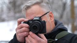 Photographer holding a Nikon Z mirrorless camera up to his face while wearing glasses and dark winter clothing.