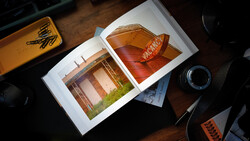 Open portfolio displaying architectural photography prints on a wooden desk with camera equipment nearby.