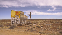 Weathered yellow roadside sign structure standing alone in vast, flat desert landscape under dramatic sky.