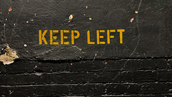 Yellow "KEEP LEFT" text painted on weathered black asphalt surface.