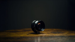 Black camera lens with orange reflections positioned on a wooden surface against a dark background.