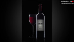 Wine bottle and filled glass against a black background with dramatic side lighting.