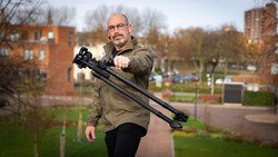 Man holding a camera stabilizer rig with mounted camera and lens in an urban park setting.