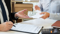 Two people exchanging cash and documents at a desk during a business transaction.