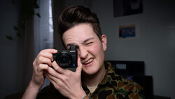 Person holding a Sony compact camera up to their face, smiling while framing a shot.