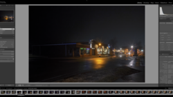 Night photograph of an illuminated commercial building with warm lighting reflected on wet pavement.